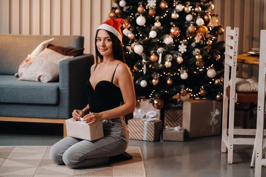 A girl with a new year's gift in her hands is sitting at home near the Christmas tree.