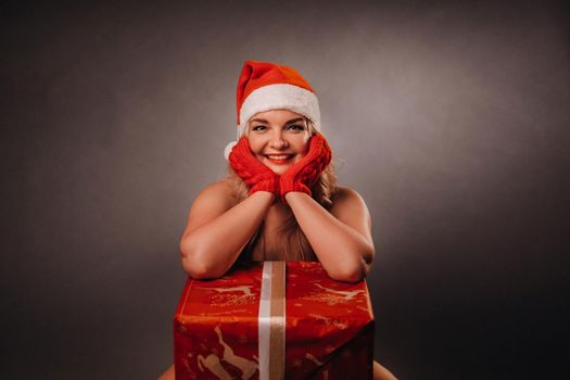 undressed girl in a Christmas hat sits with a gift in a black background.