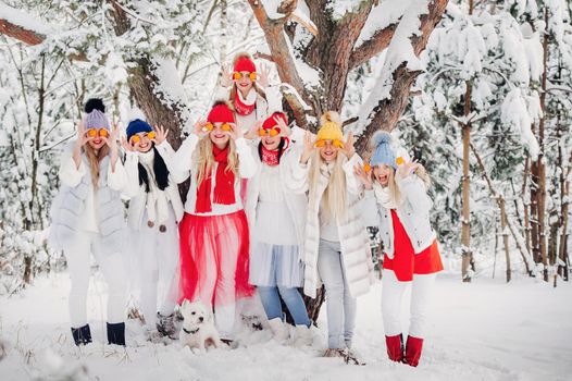 A large group of girls with tangerines are standing in the winter forest.Girls in red and white clothes with fruit in a snow-covered forest.