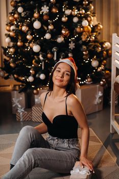 A girl with a new year's gift in her hands is sitting at home near the Christmas tree.