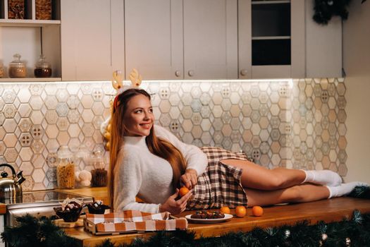 A girl at Christmas is lying on the kitchen table and holding a tangerine in her hands.Woman on new year's eve in the kitchen lying with horns.