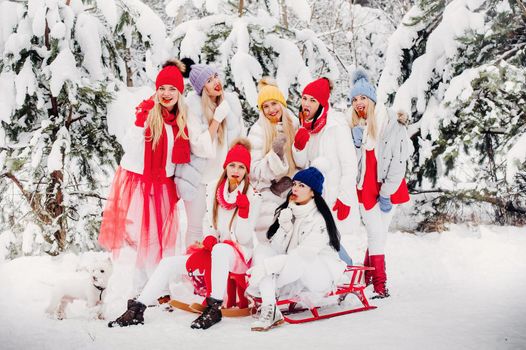 A large group of girls with lollipops in their hands stands in the winter forest.Girls in red and white clothes with candy in a snow-covered forest