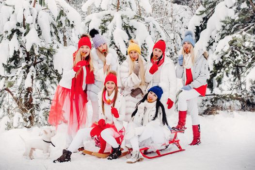 A large group of girls with lollipops in their hands stands in the winter forest.Girls in red and white clothes with candy in a snow-covered forest