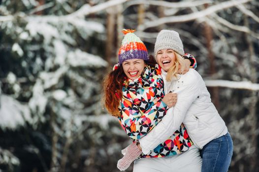 Two girls in the winter forest emotionally hug and smile.Happy women hug and Express joy.