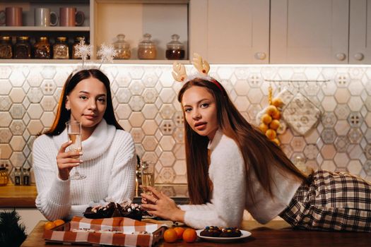 two girls in a cozy home environment with champagne in their hands at Christmas. Smiling girls drink champagne on a festive evening.