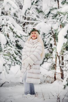 Portrait of a woman in a white fur coat in a cold winter forest. Girl with a wreath on her head in a snow-covered winter forest.