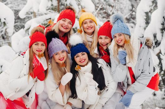 A large group of girls with lollipops in their hands stands in the winter forest.Girls in red and white clothes with candy in a snow-covered forest