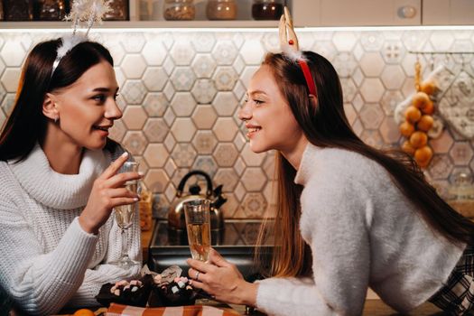 two girls in a cozy home environment with champagne in their hands at Christmas. Smiling girls drink champagne on a festive evening.
