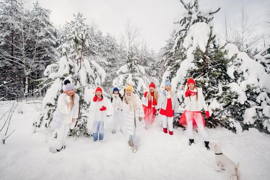 A large group of girls with lollipops in their hands stands in the winter forest.Girls in red and white clothes with candy in a snow-covered forest