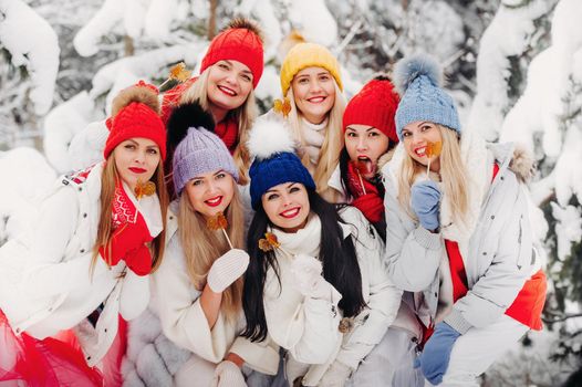 A large group of girls with lollipops in their hands stands in the winter forest.Girls in red and white clothes with candy in a snow-covered forest