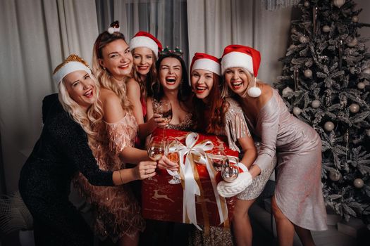 sexy women in Santa hats with glasses of champagne and a big gift. New year holiday. Christmas eve. On the background of the home interior. Happy New Year.