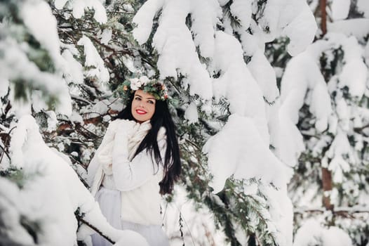 PPortrait of a woman in white clothes in a cold winter forest. Girl with a wreath on her head in a snow-covered winter forest.