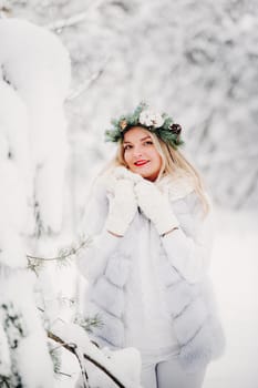 PPortrait of a woman in white clothes in a cold winter forest. Girl with a wreath on her head in a snow-covered winter forest.