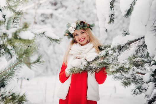 Portrait of a woman in a red jacket in a cold winter forest. Girl with a wreath on her head in a snow-covered winter forest.