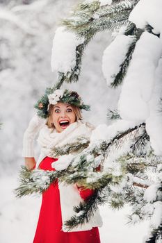 Portrait of a woman in a red jacket in a cold winter forest. Girl with a wreath on her head in a snow-covered winter forest.