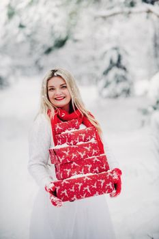 A girl in a white sweater with Christmas gifts in her hands stands in a snow-covered forest.Woman with Christmas gifts outside in winter.