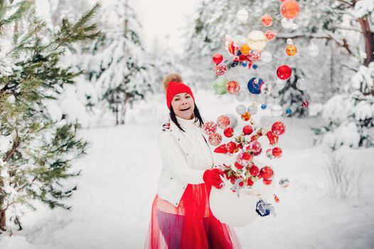 A girl in a white jacket throws Christmas balls to decorate the Christmas tree.A girl throws Christmas decorations from a basket into the winter forest.