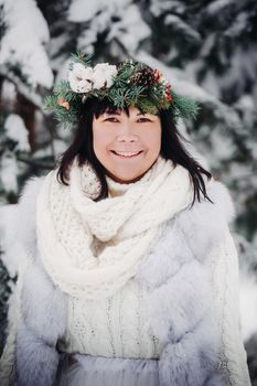 Portrait of a woman in white clothes in a cold winter forest. Girl with a wreath on her head in a snow-covered winter forest