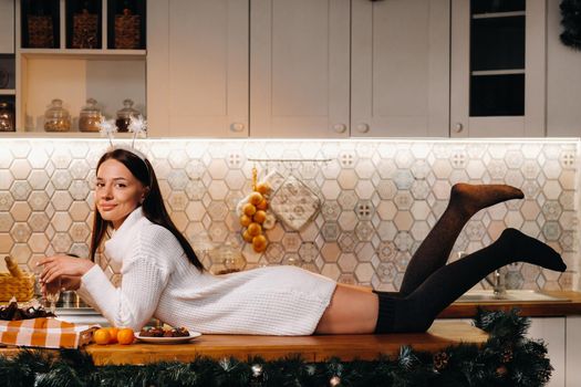 A girl at Christmas is lying on the kitchen table and holding a glass of champagne.Woman on new year's eve with champagne.