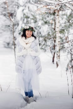 Portrait of a woman in white clothes in a cold winter forest. Girl with a wreath on her head in a snow-covered winter forest