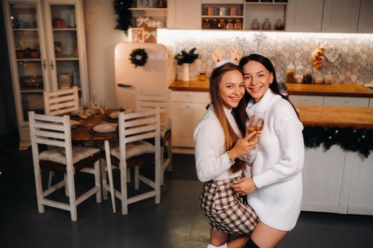 two girls in a cozy home environment with champagne in their hands at Christmas. Smiling girls drink champagne on a festive evening.