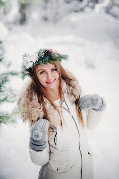 Portrait of a woman in white clothes in a cold winter forest. Girl with a wreath on her head in a snow-covered winter forest.