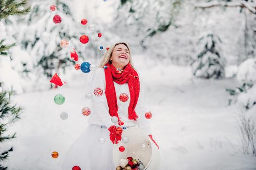A girl in a white jacket throws Christmas balls to decorate the Christmas tree.A girl throws Christmas decorations from a basket into the winter forest.