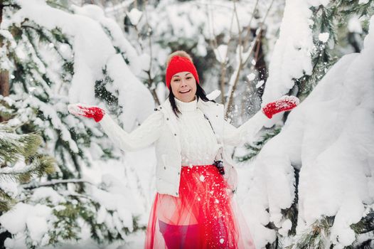 Portrait of a woman in white clothes and a red hat in a cold winter forest. Girl in a snow-covered winter forest.