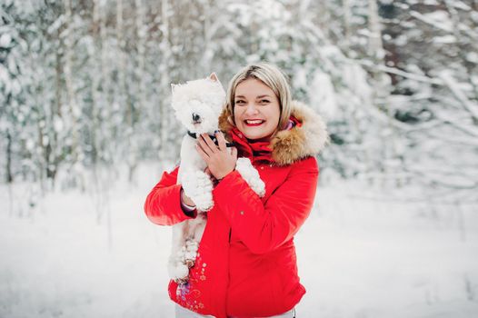 Portrait of a woman in a red jacket with a dog in a cold winter forest. A girl holds a dog in her hands in a snow-covered winter forest