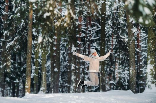 a woman in gray clothes jumps emotionally in a winter forest.Girl in the new year's snow-covered forest