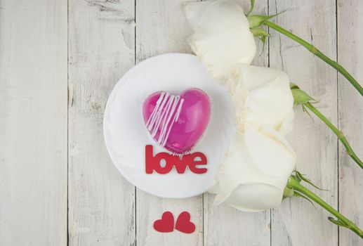 word love and white petals rose with red cake in the shape of a heart is on the table. Romantic date. 