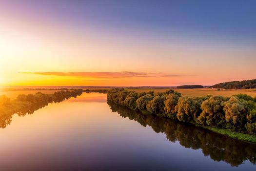 A sunset or sunrise scene over a lake or river with skies reflecting in the water on a summer evening or morning. Landscape.