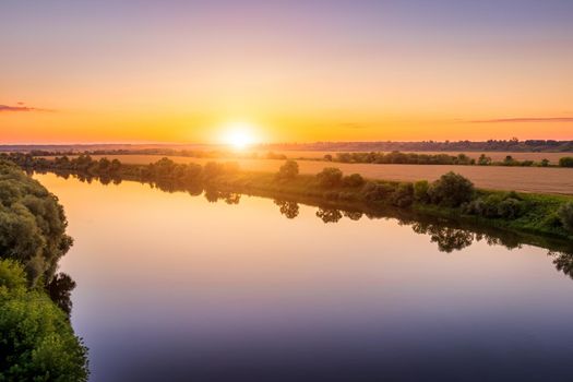 A sunset or sunrise scene over a lake or river with skies reflecting in the water on a summer evening or morning. Landscape.