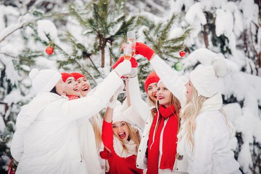 A large group of girls with glasses of champagne in their hands stands in the winter forest.Girls in red and white clothes with new year's drinks in a snow-covered forest