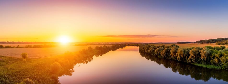 A sunset or sunrise scene over a lake or river with skies reflecting in the water on a summer evening or morning. Panorama.