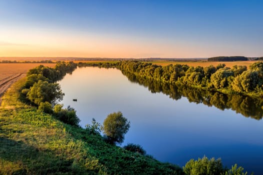 A sunset or sunrise scene over a lake or river with skies reflecting in the water on a summer evening or morning. Landscape.