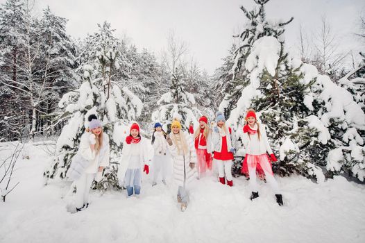 A large group of girls with lollipops in their hands stands in the winter forest.Girls in red and white clothes with candy in a snow-covered forest