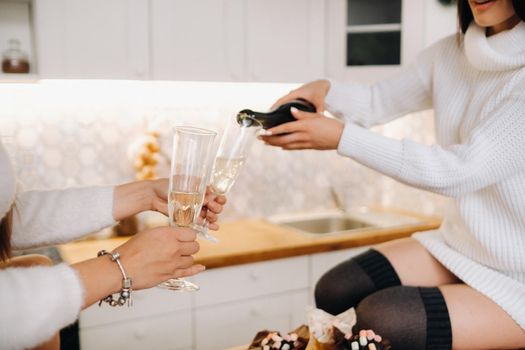 two girls in a cozy home environment in the kitchen pour champagne for Christmas. Smiling girls drink champagne on a festive evening.