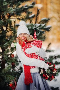 A girl in a white sweater with Christmas gifts in her hands stands in a snow-covered forest.Woman with Christmas gifts outside in winter