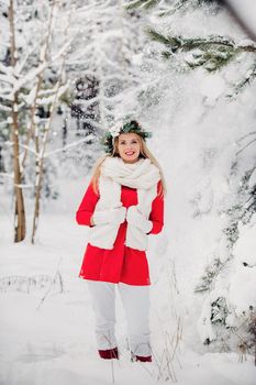 Portrait of a woman in a red jacket in a cold winter forest. Girl with a wreath on her head in a snow-covered winter forest.