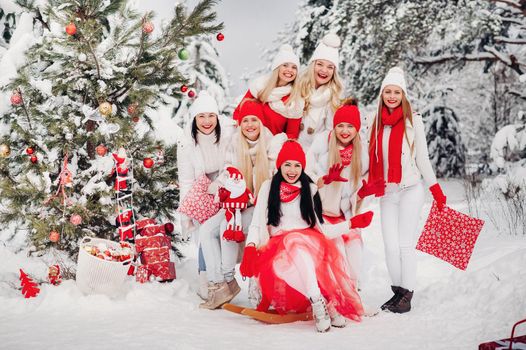 A large group of girls with Christmas gifts in their hands standing in the winter forest.Girls in red and white clothes with Christmas gifts in the snowy forest.