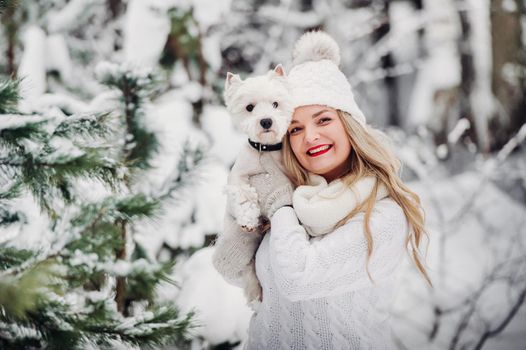 Portrait of a woman in a white sweater with a dog in a cold winter forest. A girl holds a dog in a snow-covered winter forest.