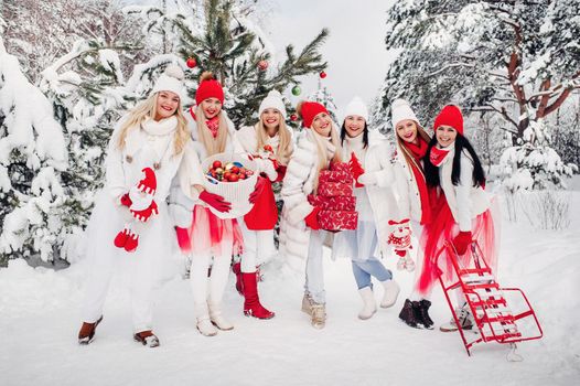 A large group of girls with Christmas gifts in their hands standing in the winter forest.Girls in red and white clothes with Christmas gifts in the snowy forest