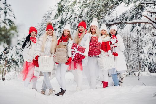 A large group of girls with Christmas gifts in their hands standing in the winter forest.Girls in red and white clothes with Christmas gifts in the snowy forest.