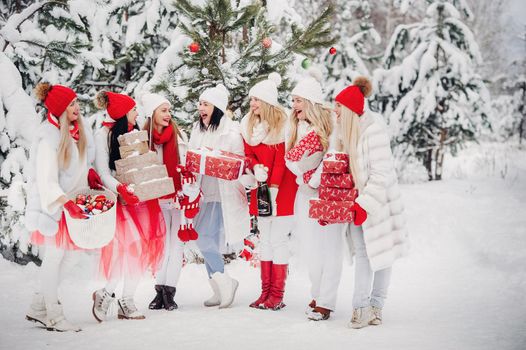 A large group of girls with Christmas gifts in their hands standing in the winter forest.Girls in red and white clothes with Christmas gifts in the snowy forest.