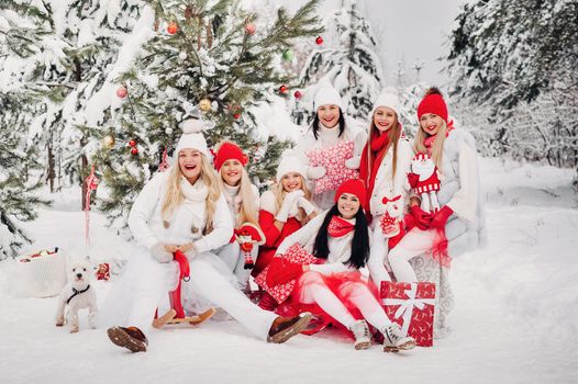 A large group of girls with Christmas gifts in their hands standing in the winter forest.Girls in red and white clothes with Christmas gifts in the snowy forest