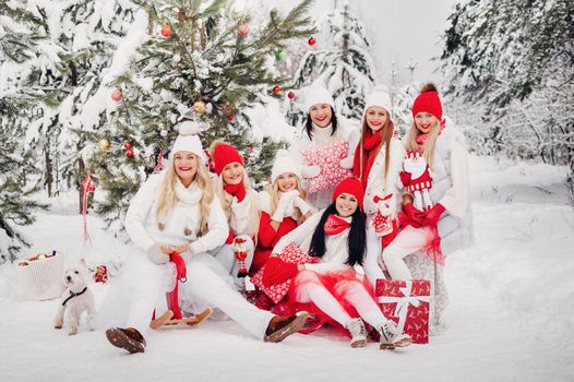 A large group of girls with Christmas gifts in their hands standing in the winter forest.Girls in red and white clothes with Christmas gifts in the snowy forest