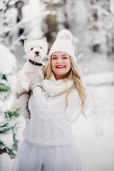Portrait of a woman in a white sweater with a dog in a cold winter forest. A girl holds a dog in a snow-covered winter forest.