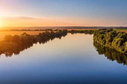 A sunset or sunrise scene over a lake or river with skies reflecting in the water on a summer evening or morning. Landscape.