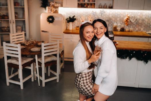 two girls in a cozy home environment with champagne in their hands at Christmas. Smiling girls drink champagne on a festive evening.